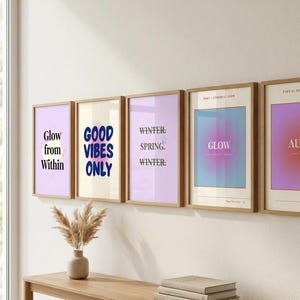 Könnte beinhalten: Eine Sammlung gerahmter Kunstdrucke mit inspirierenden Zitaten und abstrakten Designs. Die Drucke zeigen Texte wie "Glow from Within" und "Good Vibes Only" in verschiedenen Schriftarten und Farben. Eine Holzkonsolentisch mit einer Vase und Büchern befindet sich im Vordergrund.