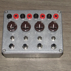 May include: A silver metal box with a variety of knobs, switches, and jacks. The box has a red, black, and white color scheme.