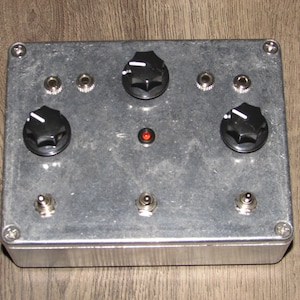May include: A silver metal box with three knobs and three jacks. The box has a red LED light on the front.