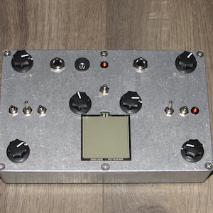 May include: A silver metal effects pedal with black knobs, switches, and a small LCD screen. The screen displays the text "MIDI VELOCITY RAM".