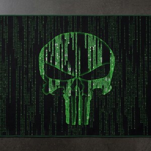 May include: A rectangular black mat featuring a large, central skull graphic composed of vertical green digital code characters. The background consists of a repeating pattern of cascading green symbols, creating a matrix-like aesthetic across the surface.