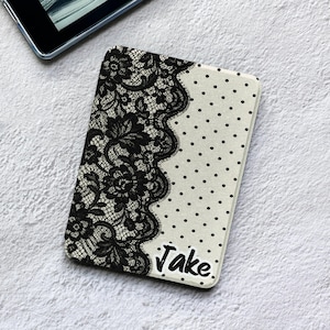 May include: A rectangular e-reader case featuring a split design with black floral lace patterns on the left side and a cream-colored background with black polka dots on the right side. The name Jake is printed in black script in the bottom corner.