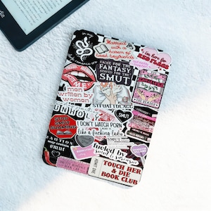 May include: A black and white e-reader cover adorned with numerous stickers. The stickers feature phrases like "Smut," "Red Flags," and "Touch Her & Die Book Club." A portion of a black e-reader is visible in the upper left corner.