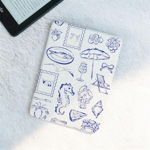 May include: A white e-reader cover featuring a blue nautical design. The pattern includes illustrations of a seahorse, fish, umbrella, and other beach-related images. A black e-reader is visible nearby.
