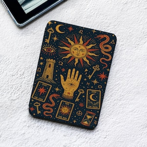 May include: A rectangular e-reader cover featuring a dark blue background with gold and orange illustrations of a sun, a hand with an eye, snakes, keys, a tower, an hourglass, and tarot cards labeled The Star, The Moon, and The Sun.