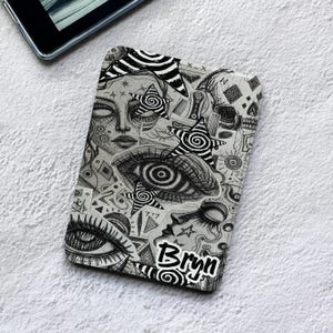 Pode incluir: Uma capa retangular para leitor de e-books com uma ilustração detalhada em tinta preta e branca de rostos, olhos e estrelas giratórias. O design inclui vários padrões geométricos e o nome Bryn impresso em fonte preta com contorno branco.