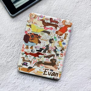 Puede incluir: Una funda rectangular para lector electrónico con fondo blanco y un patrón repetitivo de perros salchicha en varias posturas, con accesorios como gafas en forma de estrella y jerséis, intercalados con pequeños iconos y el nombre Evan en cursiva.