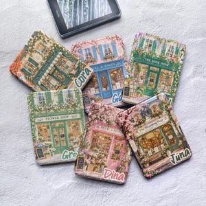 May include: Six rectangular e-reader cases featuring illustrated storefronts with floral accents. The cases display text including The Story Nook, Cora, Pages, The Book Nook, Flower Shop, Petal & Bloom, Dina, The Blooming Page, and Juna.
