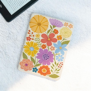 May include: A cream-coloured Kindle cover adorned with a colourful floral pattern. The design includes yellow, orange, pink, purple, and blue flowers. An e-reader is visible in the top left corner, suggesting the cover's protective function.
