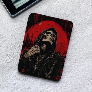 May include: A rectangular e-reader cover featuring a graphic illustration of a hooded skeleton wearing a black leather jacket with studs and a chain necklace. The background is a vibrant red circle with silhouettes of industrial structures and birds.