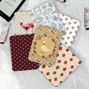 Può includere: Una collezione di sei custodie rettangolari per e-reader con vari motivi, tra cui un'oca bianca in una ghirlanda floreale, cuori rossi su fondo bordeaux, fragole rosse su crema, disegni a linee blu e bicchieri da cocktail.