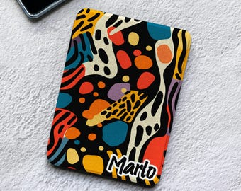 Puede incluir: Una funda rectangular para lector electrónico con un patrón abstracto vibrante de formas negras, naranjas, amarillas, azules y crema. El diseño incluye manchas, rayas y formas orgánicas. El nombre Marlo está impreso en letras blancas abajo.