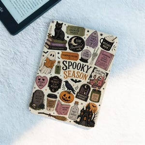 May include: An e-reader cover featuring a cream background with a pattern of Halloween-themed illustrations including a black cat, a ghost, a pumpkin, a haunted house, and the text "SPOOKY SEASON" in the center, surrounded by various occult icons.