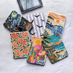 May include: Six rectangular e-reader cases featuring diverse graphic prints including a starry night with a cat, bats on stripes, a coastal sunset, floral patterns, a desert landscape with cacti, and a tropical beach scene with the names Cora, Dina, and Juna.