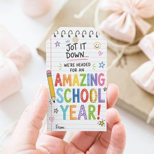 May include: A rectangular gift tag with a white lined paper background featuring a yellow pencil illustration and colourful text that reads JOT IT DOWN... WE'RE HEADED FOR AN AMAZING SCHOOL YEAR! with small hand-drawn stars, hearts, and a smiley face.