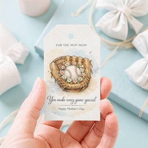 May include: A gift tag featuring a baseball glove and ball illustration, adorned with flowers. Text includes "For the MVP Mom", "You make every game special", and "Happy Mother's Day". The tag is held in a hand.