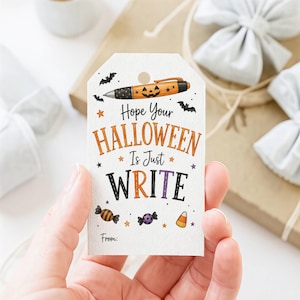 May include: A white rectangular gift tag with a hole at the top, featuring an orange jack-o'-lantern pen, bats, stars, and candy illustrations. The text reads: Hope Your HALLOWEEN Is Just WRITE. The word From: is printed at the bottom.