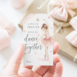 May include: A gift tag with a watercolor illustration of a ballerina in a pink tutu. The tag reads "Life is sweeter when we dance together" with a space for "From:" at the bottom. Pink hearts and watercolor accents decorate the tag.