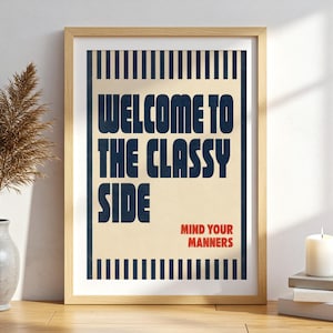 May include: A framed wall art print featuring a cream background with dark blue vertical stripes at the top and bottom. The text reads "WELCOME TO THE CLASSY SIDE" in large dark blue letters and "MIND YOUR MANNERS" in smaller red letters.
