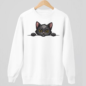May include: White sweatshirt featuring a cartoon black cat with yellow eyes and pink ears. The cat is peeking over a horizontal line. The sweatshirt has long sleeves and a crew neck, perfect for casual wear.