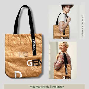 Könnte beinhalten: Eine goldfarbene Tragetasche mit schwarzen Henkeln und dem Wort "LEGEND" auf der Seite. Die Tasche ist aus einem zerknitterten Material gefertigt und hat ein minimalistisches Design.