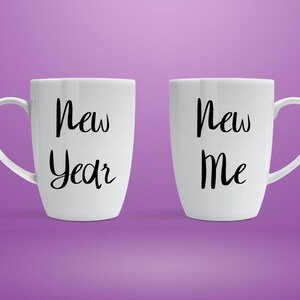 以下が含まれることがあります： 「New Year」と「New Me」という黒い文字が書かれた2つの白いセラミックマグ。マグカップには曲がったハンドルがあり、紫色の背景に配置されています。マグカップは形とサイズが同じです。