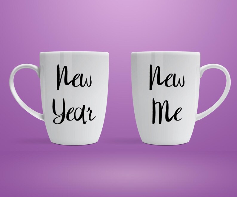 以下が含まれることがあります： 「New Year」と「New Me」という黒い文字が書かれた2つの白いセラミックマグ。マグカップには曲がったハンドルがあり、紫色の背景に配置されています。マグカップは形とサイズが同じです。