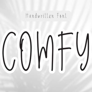 May include: A white sticker with the word "COMFY" in a handwritten black font. The word is outlined in black and set against a soft, blurred background with a palm leaf shadow. Above the word is the text "Handwritten Font".