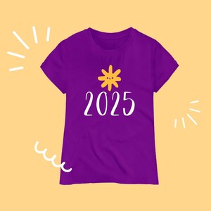 以下が含まれることがあります： 紫色のTシャツ。黄色い太陽のグラフィックと白い文字「2025」が特徴です。明るいオレンジ色の背景に白い装飾線が描かれています。