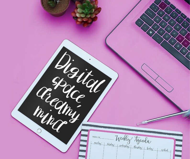 以下が含まれることがあります： ピンク色のノートパソコン、タブレット、ウィークリーアジェンダがピンク色の表面に配置されています。タブレットには、白いスクリプトで「Digital space dreamy mind」という言葉が表示されています。アジェンダは、黒と白のストライプで「Weekly Agenda」という言葉が書かれています。小さな鉢植えの植物も表示されています。