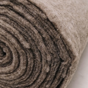 K&ouml;nnte beinhalten: Ein aufgerolltes, dickes, braunes Filzmaterial. Der Filz hat eine dichte, strukturierte Oberfl&auml;che mit sichtbaren Fasern. Die Rolle ist eng gewickelt und zeigt konzentrische Kreise des Materials. Die Farbe ist ein ged&auml;mpftes, erdiges Braun.