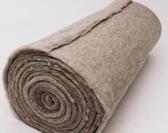 May include: A rolled-up, thick, beige fabric. The material appears to be a dense, felt-like textile, with a slightly uneven texture. The roll is tightly wound, revealing the layers of the fabric. The edges are slightly frayed.