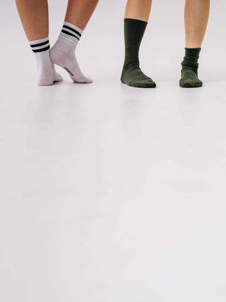 May include: Three pairs of socks in different colors. One pair is white with black stripes, another is light pink, and the last two pairs are dark green. The socks are worn by three people, with their legs and feet visible.