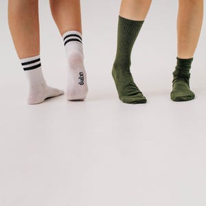 May include: Three pairs of socks in the image. One pair is white with black stripes, another is olive green, and the third is a darker olive green. The socks are worn by three people. The brand name "ukonq" is visible on one sock.