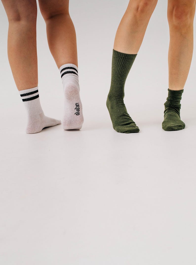 May include: Three pairs of socks in the image. One pair is white with black stripes, another is olive green, and the third is a darker olive green. The socks are worn by three people. The brand name "ukonq" is visible on one sock.