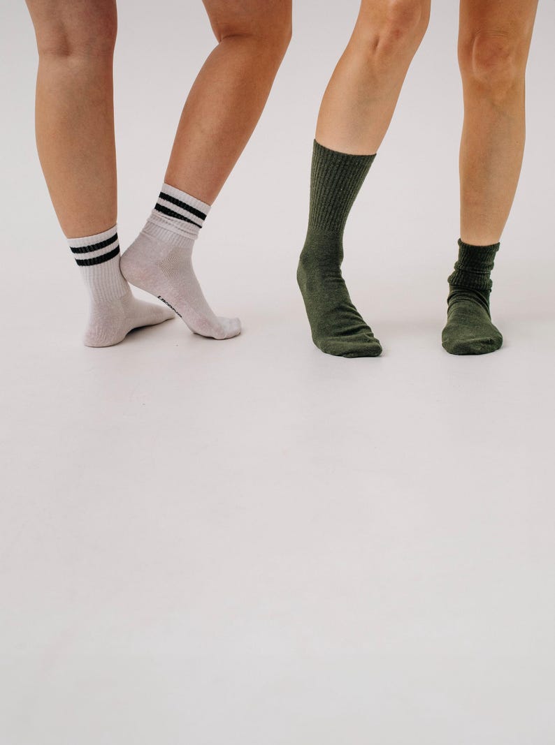 May include: Three pairs of socks are shown. One pair is light gray with black stripes at the top. The other two pairs are solid green. The socks are worn on the feet of three people.