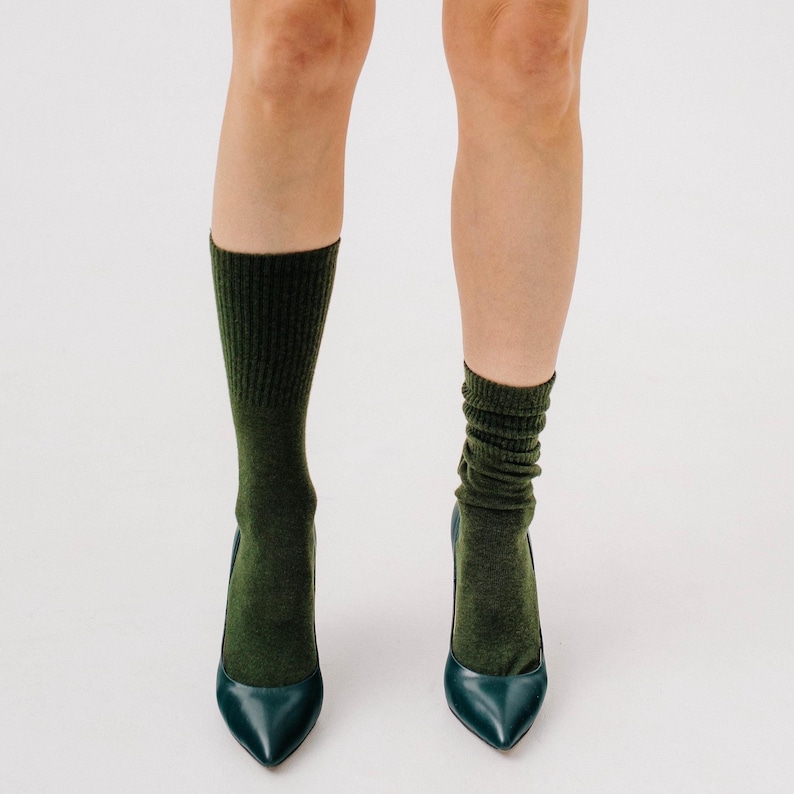May include: A pair of dark green socks paired with teal pointed-toe high heels. The socks are a solid color and reach mid-calf. The heels have a sleek, glossy finish.