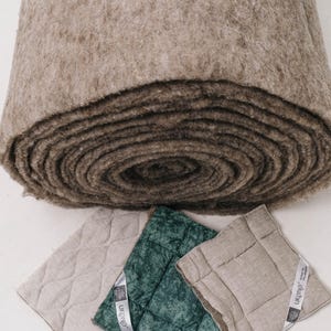 K&ouml;nnte beinhalten: Eine gro&szlig;e Rolle aus braunem Filzmaterial liegt &uuml;ber drei quadratischen, gesteppten Kissen in Beige und Gr&uuml;n. Die Kissen haben ein Rautenmuster und ein Etikett mit der Aufschrift "UKONO". Die Filzrolle scheint eine Naturfaser zu sein.