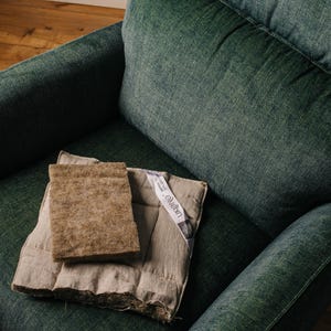 K&ouml;nnte beinhalten: Ein dunkelgr&uuml;ner Sessel mit einem hellbraunen rechteckigen Pad und einem beige gesteppten Pad. Ein wei&szlig;es Etikett mit Text ist am beigen Pad befestigt. Die Pads liegen auf dem Sitz des Sessels.