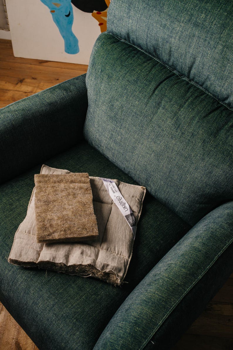 K&ouml;nnte beinhalten: Ein dunkelgr&uuml;ner Sessel mit einem hellbraunen rechteckigen Pad und einem beige gesteppten Pad. Ein wei&szlig;es Etikett mit Text ist am beigen Pad befestigt. Die Pads liegen auf dem Sitz des Sessels.