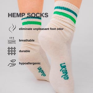 May include: Cream-colored hemp socks with green and teal stripes at the top. The text "HEMP SOCKS" is above the socks, with icons and text indicating the socks are breathable, durable, and hypoallergenic. The brand name "ukono" is printed on the side.