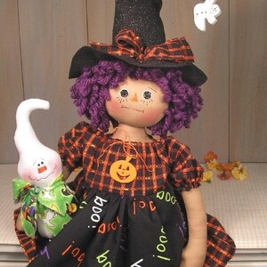 May include: A handmade witch doll with purple yarn hair, wearing a black and orange plaid dress with a black skirt that says "boo" in white and green lettering. She is holding a white ghost with a green and black bow.