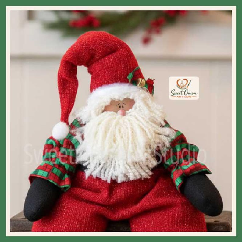 May include: A fabric Santa Claus doll wearing a red textured hat with a white pom-pom, a red textured body, and green and red plaid sleeves. The doll has a thick white yarn beard, black mittens, and a logo reading Sweet Onion Art Studio.