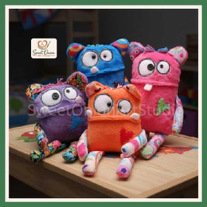 Pode incluir: Quatro monstros de pelúcia nas cores roxa, azul, laranja e rosa. Cada um apresenta grandes olhos de botão brancos, bocas costuradas e membros de tecido estampado. O logotipo da Sweet Onion Art Studio é visível no canto superior esquerdo.