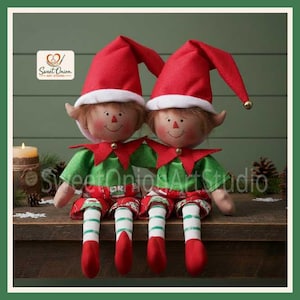 May include: Two plush elf dolls with tan skin, rosy cheeks, and brown hair. They wear red pointed hats with white trim, green shirts with red collars, and red and white striped pants with red shoes. A logo reads Sweet Onion Art Studio.