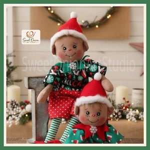 Op de afbeelding: Twee pluche elfpoppen met beige stoffen huid, roze wangen en puntige oren. De grotere pop draagt een rode muts, een zwart shirt met kerstpatronen en een rode broek met stippen. De kleinere pop draagt een rode muts en een groen shirt met witte patronen.