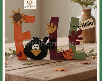 May include: A decorative wooden sign spelling FALL with an orange F, a black bird replacing the A, a maroon L, and a green L. The letters feature autumn-themed cutouts including a sunflower, leaves, and a small tag with the text Hello attached.