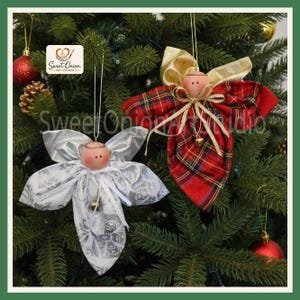 May include: Two handmade angel ornaments hanging on a Christmas tree. One angel features a white fabric with a silver floral pattern, while the other displays a red and green plaid fabric with gold ribbon accents. Both have round wooden heads.
