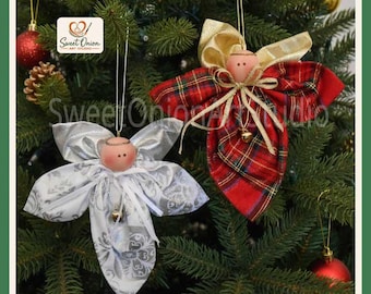 May include: Two handmade angel ornaments hanging on a Christmas tree. One angel features a white fabric with a silver floral pattern, while the other displays a red and green plaid fabric with gold ribbon accents. Both have round wooden heads.