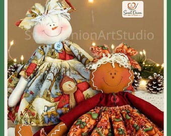 May include: Two fabric dolls with stitched facial features and yarn hair. The left doll wears a blue patterned dress with a snowman print. The right doll has a brown face and wears a dark red top with a patterned skirt featuring green accents.
